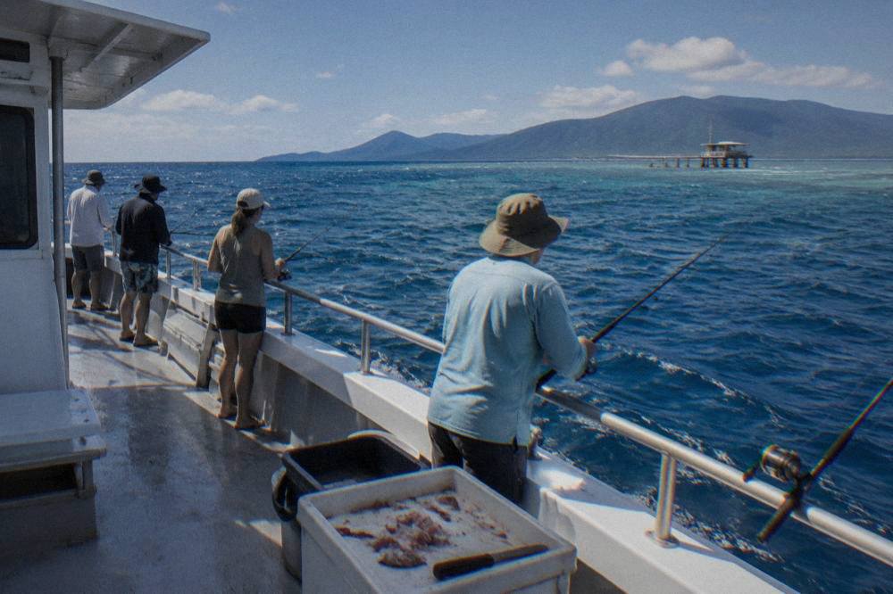 Anglers fishing with rods over the side of a charter boat on open blue reef water